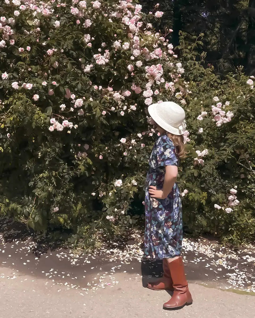 Young girl in navy floral dress, ivory straw hat helmet cover, brown boots